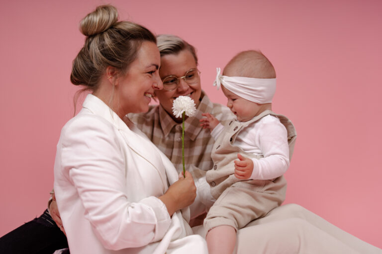 Eltern posieren vor einem pinken Hintergrund mit ihrem Baby. - Familienshooting als Geschenk