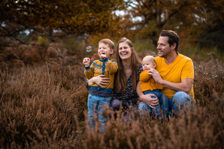 Foto einer Famile in der Natur. Die zwei Eltern lachen entspannt mit ihren zwei Kindern auf dem Bild. - Familienshooting mit Kindern
