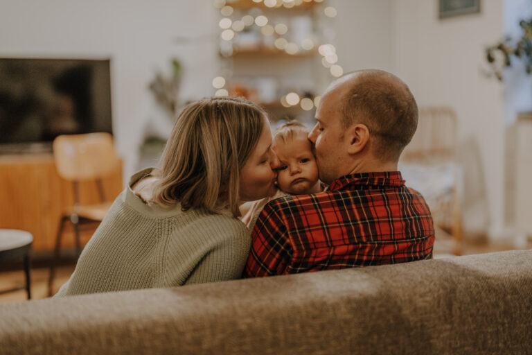 Eltern sitzen mit ihrem Baby auf dem Sofa und werden von hinten fotografiert. - Newborn Shooting Köln