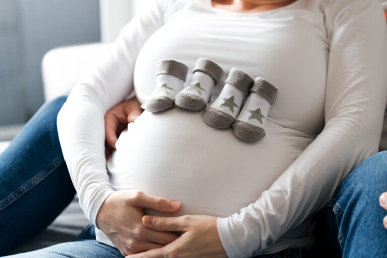 Fokus auf einen schwangeren Bauch, auf dem 4 kleine Söckchen liegen. - Schwangerschaftsfotos Köln