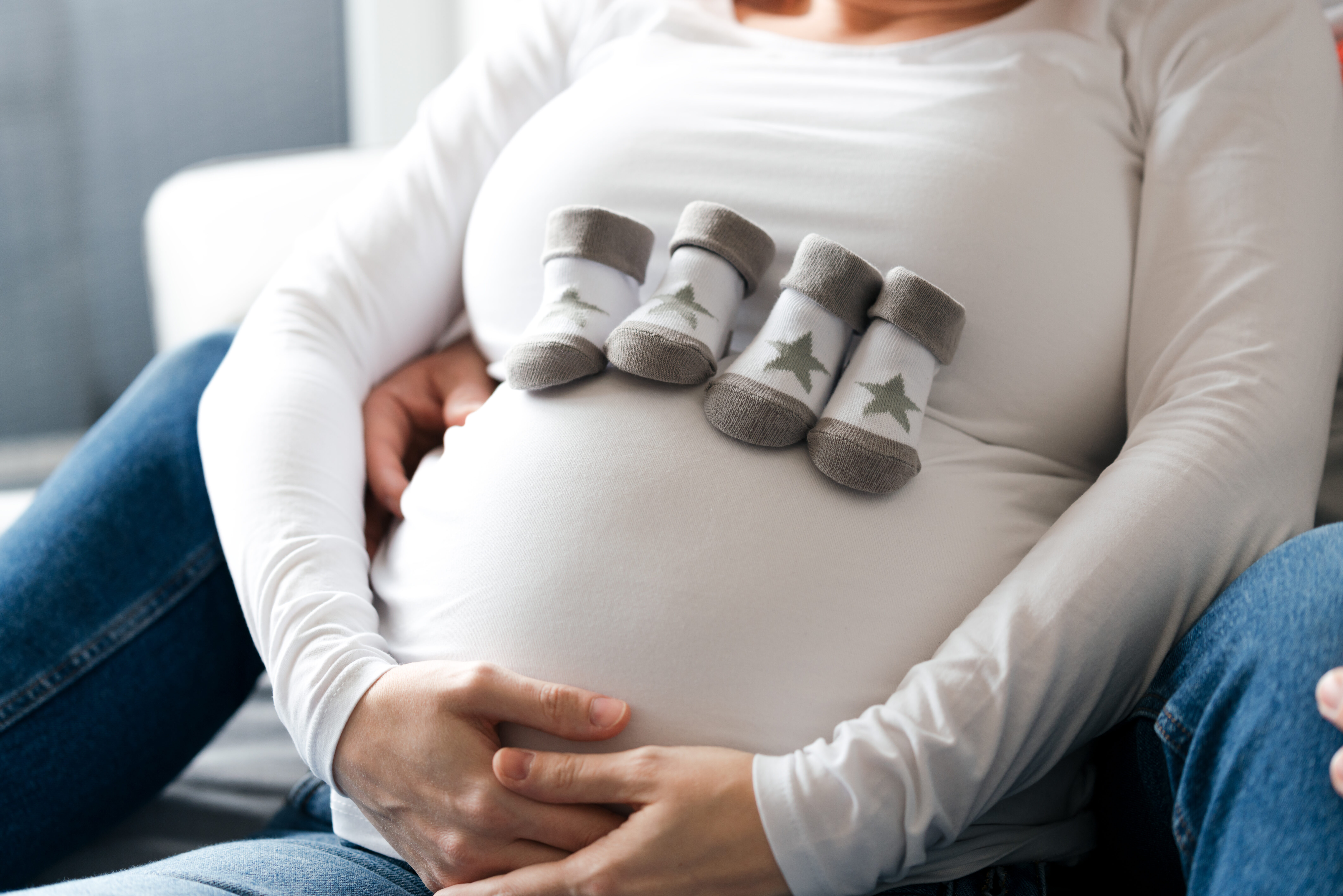 Fokus auf einen schwangeren Bauch, auf dem 4 kleine Söckchen liegen. - Schwangerschaftsfotos Köln