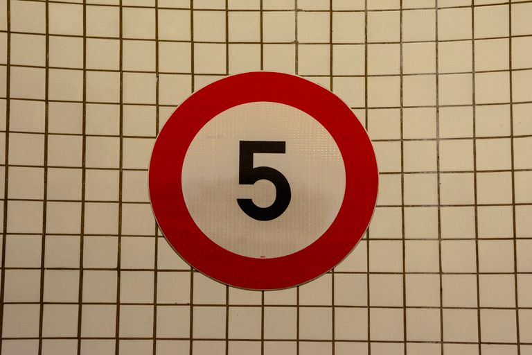 Close-up of a speed limit sign with the number 5 against a tiled wall background.