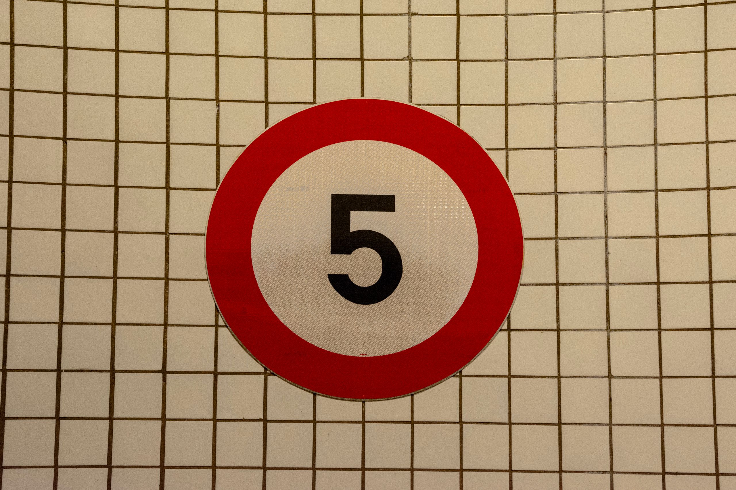 Close-up of a speed limit sign with the number 5 against a tiled wall background.