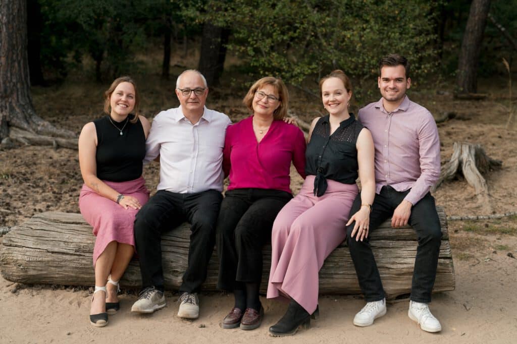 Familienfoto von Eltern mit ihren erwachsenen Kindern, die auf einem Baumstamm sitzen.